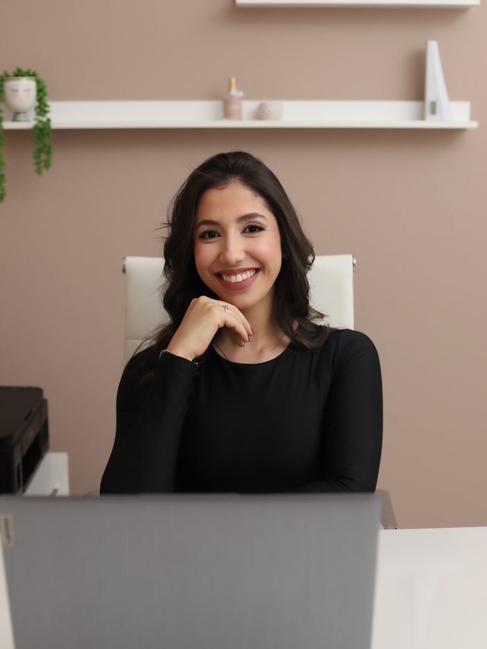 Katryne Azevedo sorrindo à mesa do consultório, em frente ao notebook